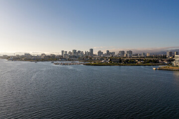 Obraz premium Oakland California waterfront presenting its downtown skyline with modern buildings, a bustling marina, the bay, and distant fog under a clear sky