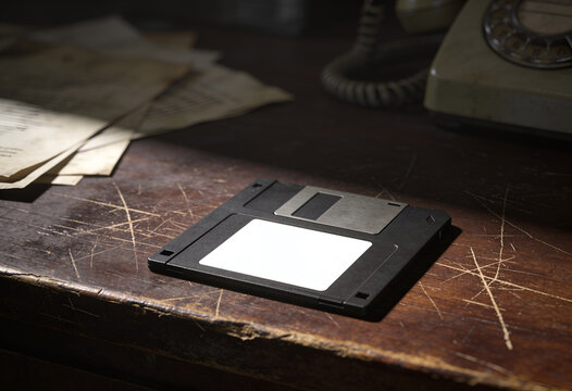 Vintage floppy disk on a scratched wooden desk with old papers and phone