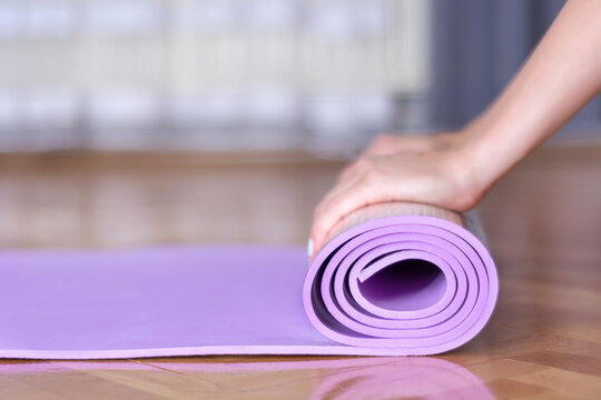 close-up of female hand rolling purple yoga mat on wooden floor