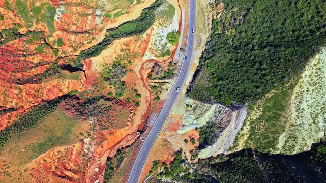 Scenic highway winding through vibrant colored sandstone canyons and green hills in Xinjiang, China.