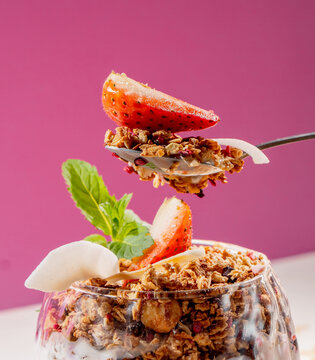 Healthy Granola Yogurt Parfait with Fresh Strawberry, Mint and Coconut Flakes on Pink Background