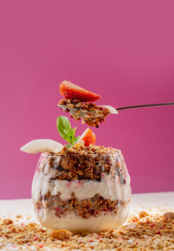 Healthy Granola Yogurt Parfait with Fresh Strawberry, Mint and Coconut Flakes on Pink Background