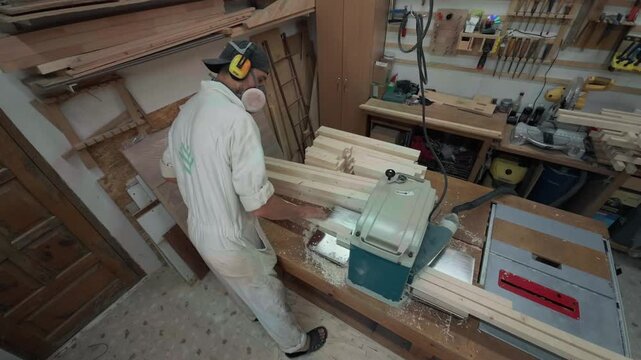 Unrecognizable Millwork Craftsman Feeding Solid Timber Blanks Into Heavy Thickness Planer Machine During Precision Joinery Process In Organized Workshop High Angle Over The Shoulder Authentic B-Roll