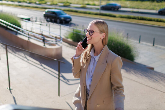 young blonde businesswoman walks up outdoor steps while talking on her phone