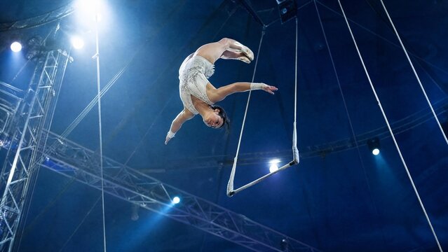 Graceful Female Aerialist Performing Acrobatics on Trapeze in Circus Arena
