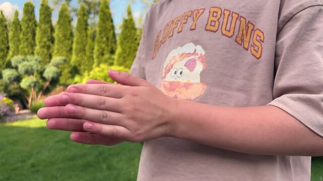 Person clapping hands outdoors wearing a brown t-shirt