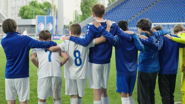 Football team players stand and hug while waiting for a penalty kick to be taken against them, view from behind
