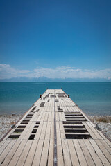 Fototapeta premium Wooden Pier Extending into Calm Blue Lake with Mountain Landscape and Clear Sky