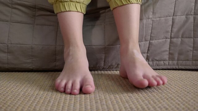 Child's bare feet dangling and swinging from a bed. Close-up view of a child's bare feet dangling and swinging playfully after getting out of bed in the morning, representing a carefree and relaxed