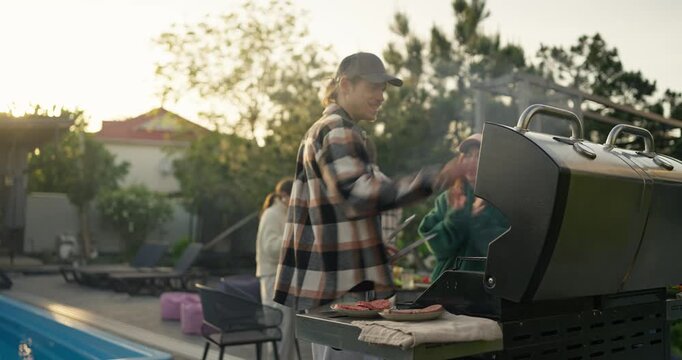 Man grilling outdoors beside a pool at sunset
