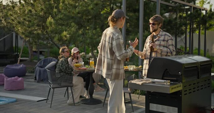 Friends socializing around a backyard barbecue on a sunny patio