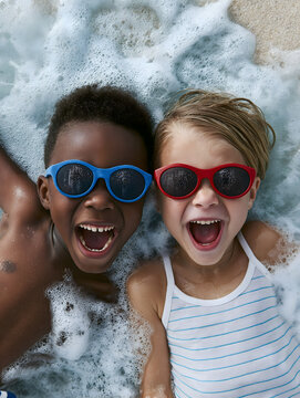 Two young friends are having a wonderful time playing with the waves at the water's edge on a beach.