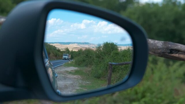 Truck overtaking maneuver on scenic tuscan road in rearview mirror. Wing mirror reflecting a truck performing an overtaking maneuver on a picturesque tuscan road, with rolling hills and blue skies