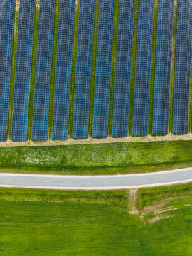 Aerial view of rows of solar panels in a green field next to a road in Suntazi, Ogre Municipality, Latvia.