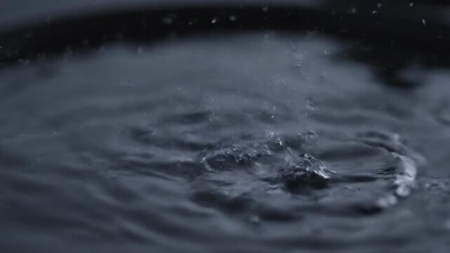Close-up of water droplet impact creating a splash in a reflective, dark liquid surface