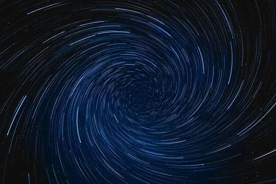 A long-exposure photograph showing spiral-shaped star trails in a dark night sky, capturing celestial rotation.