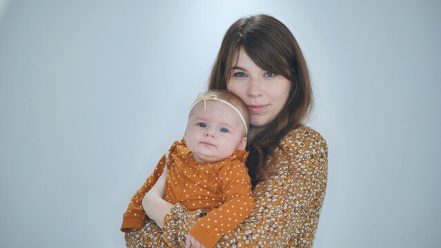 Loving mother embracing newborn daughter in coordinating orange toned outfits during intimate studio photography session