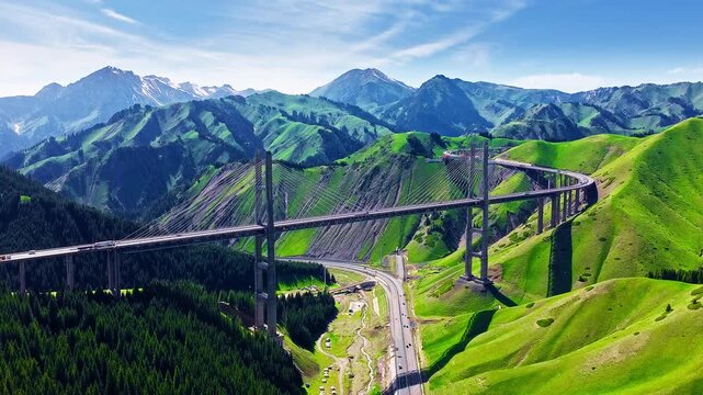 Aerial view of Guozigou Bridge spanning across lush green mountains in Xinjiang, China, showcasing spectacular infrastructure and scenic natural landscape.