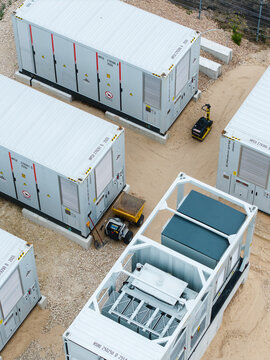Aerial view of industrial battery energy storage system containers placed on a gravel site with electrical equipment and a small compacting machine in Suntazi, Ogre Municipality, Latvia.