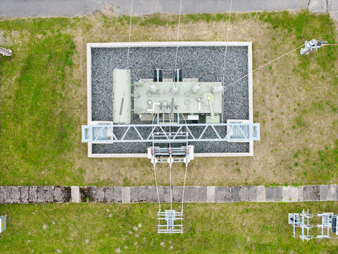 Aerial view of an electrical transformer station with metal framework and power lines set within a gravel enclosure surrounded by green grass in Suntazi, Ogre Municipality, Latvia.