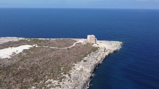 Aerial view of the historic Xlendi Tower standing on a rocky peninsula overlooking the blue Mediterranean Sea and coastal cliffs in Munxar, Gozo Region, Malta. High quality 4k footage
