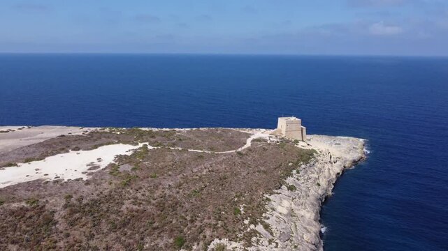 Aerial view of the historic Xlendi Tower standing on a rocky peninsula overlooking the blue Mediterranean Sea and coastal cliffs in Munxar, Gozo Region, Malta. High quality 4k footage