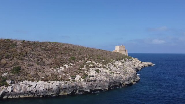 Aerial view of the historic Xlendi Tower standing on a rocky peninsula overlooking the blue Mediterranean Sea and coastal cliffs in Munxar, Gozo Region, Malta. High quality 4k footage