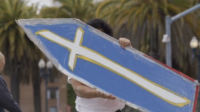 Man Swinging Painted Board Overhead In San Francisco Plaza - Medium Slow Motion Shot