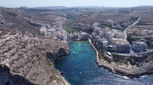 Aerial view of Xlendi Bay featuring the historic watchtower on the rocky cliffs and coastal buildings in Munxar, Gozo Region, Malta. High quality 4k footage