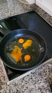 Slow motion close up of cracking eggs onto hot frying pan on stove