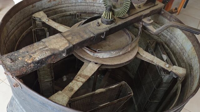 Vintage manual honey extractor machine inside a local honey shop, close-up of old mechanical gears and rustic metal drum.