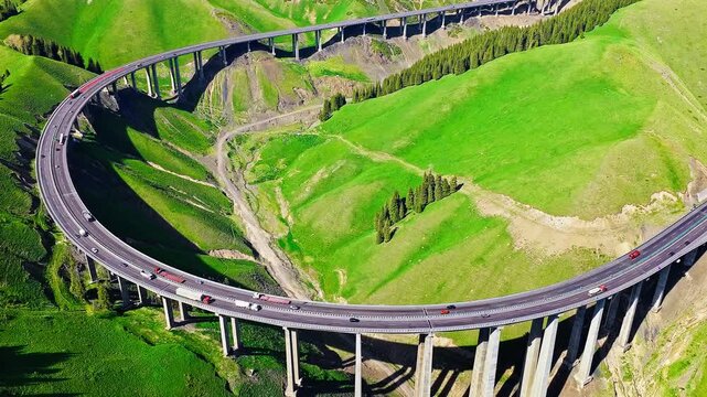 Aerial view of Guozigou Bridge winding through green mountains in Xinjiang, China.