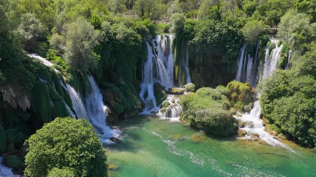 Aerial drone panorama of spectacular cascading waterfalls surrounded by lush green forest and clear river