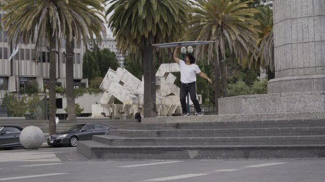 Man Tossing Flat Board Skyward And Other Tricks As He Stands On Granite Plaza Steps - Wide Shot