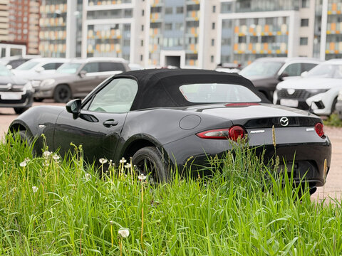 A stylish Mazda MX-5 RF Miata Sport Tech, two door sports car convertible black color, in a carpark at the city. Exterior of a Mazda MX-5 Miata RF Roadster fastback model. JDM car. 