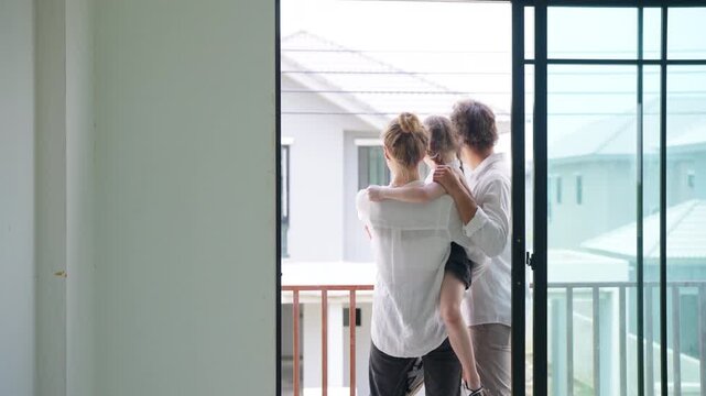 Happy family viewing unfinished new home in residential housing development. Parents and daughter standing on balcony of house under construction before moving into future property