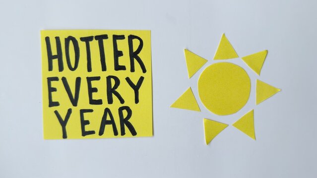 Yellow sticky note says 'HOTTER EVERY YEAR' beside sun cutout. Minimalist white background shows climate change message. Ideal for environmental campaigns or educational materials