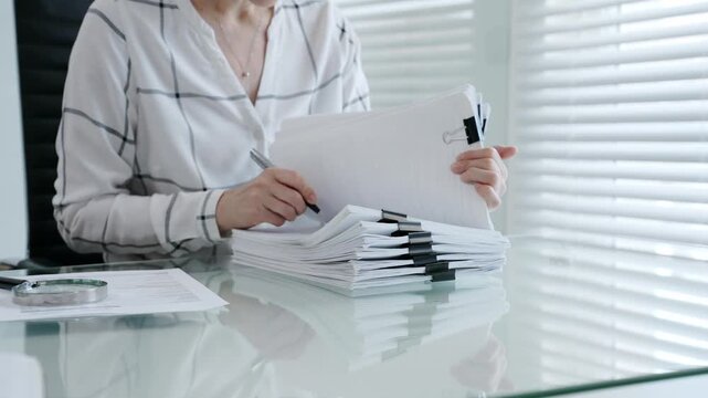 Financial auditor reviewing company documents, checking tax compliance reporting, conducting a detailed investigation, and thoroughly analyzing business paperwork for legal adherence