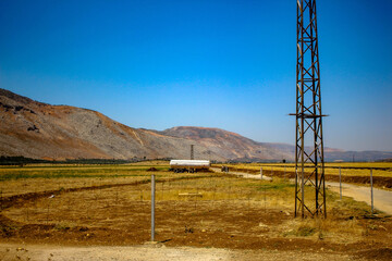 Fototapeta premium Industrial power transmission tower in a rural valley with a tanker truck on a dusty road