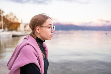 Side profile portrait of a teenage girl in glasses by the calm sea at sunset. © Lena May