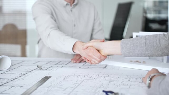 Handshaking between two architects finalizing a construction project deal, business partners agreeing on engineering blueprints and architectural models in an office, close up