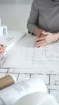 Architects discussing modern building design with 3d model and blueprints during planning meeting focused on innovation, teamwork and sustainable construction solutions, close up