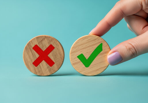 Hand placing wooden token with check mark symbol next to one with cross sign illustrating decision making process on turquoise background view.