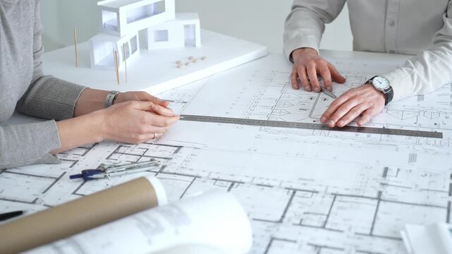 Architects discussing architectural blueprints and a building model on a white desk, planning a new construction project and developing innovative design solutions collaboratively, close up