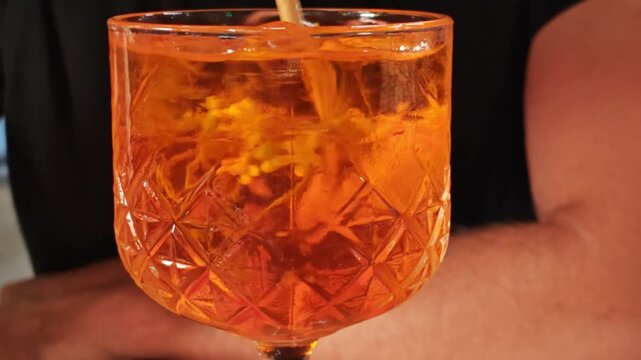 Stirring ice with fruit in a glass with an aperol cocktail