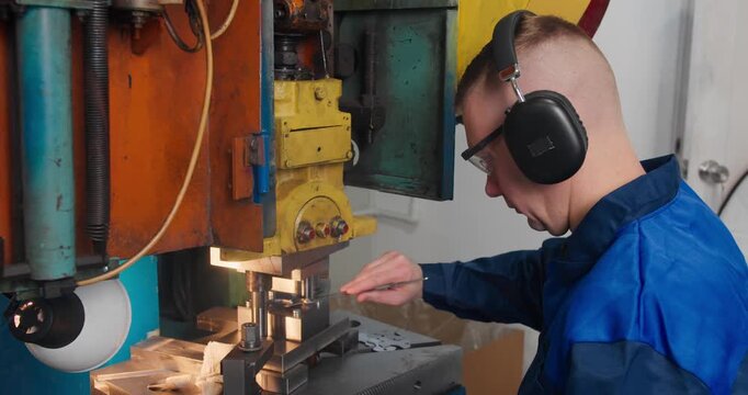 Factory worker operating industrial press machine in manufacturing workshop. Blue collar employee working with metal parts