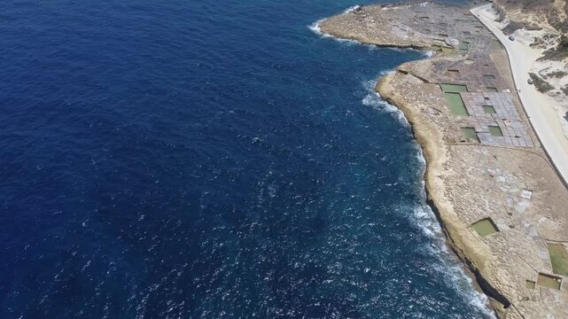 Xwejni s centuries-old salt pans unfold along the rugged coast of Zebbug, Gozo, geometric pools and vivid Mediterranean blues in a sweeping summer Aerial view. High quality 4k footage