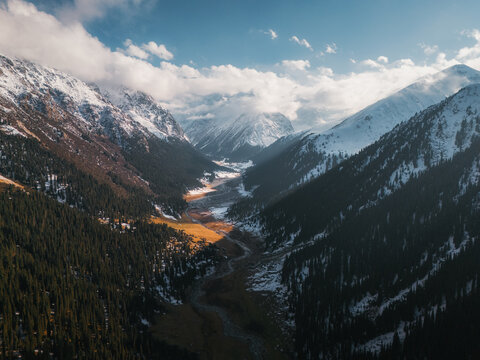 Aerial view of the majestic Boris Yeltsin Peak towering over snow-dusted coniferous forests and a winding river in the valley, Jety-Oguz, Issyk-Kul Region, Kyrgyzstan.