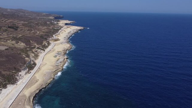 Xwejni s centuries-old salt pans unfold along the rugged coast of Zebbug, Gozo, geometric pools and vivid Mediterranean blues in a sweeping summer Aerial view. High quality 4k footage