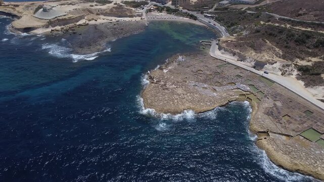 Xwejni s centuries-old salt pans unfold along the rugged coast of Zebbug, Gozo, geometric pools and vivid Mediterranean blues in a sweeping summer Aerial view. High quality 4k footage
